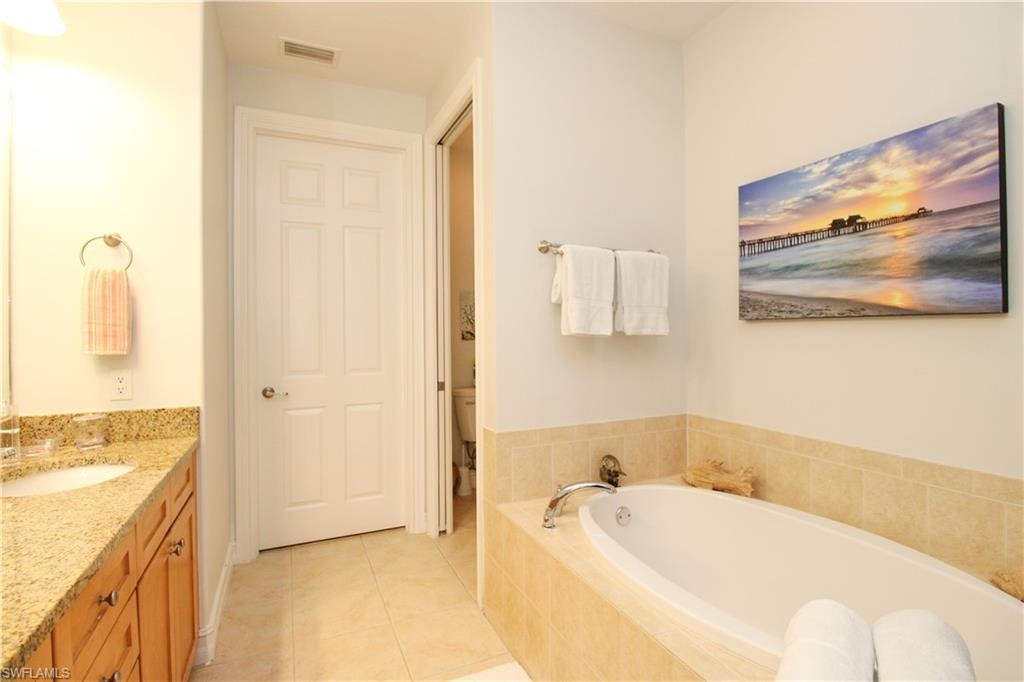 Bathroom featuring vanity, toilet, tile patterned floors, and tiled bath