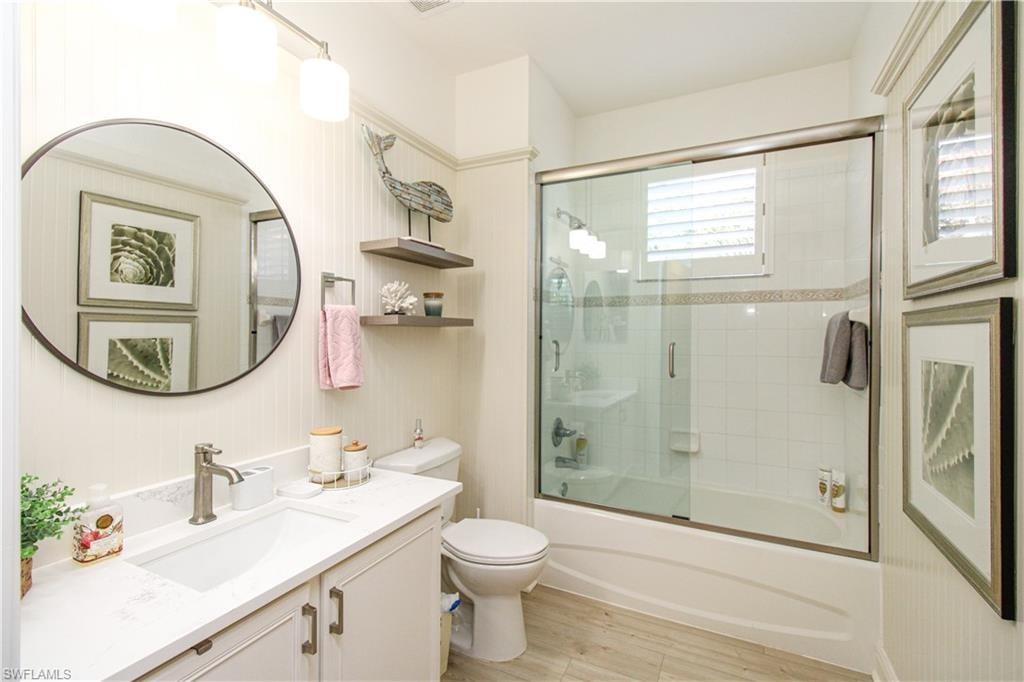 Full bathroom with toilet, combined bath / shower with glass door, vanity, and wood-type flooring