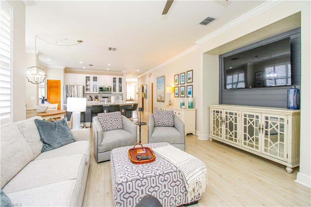 Living room with ornamental molding, a notable chandelier, and light hardwood / wood-style floors