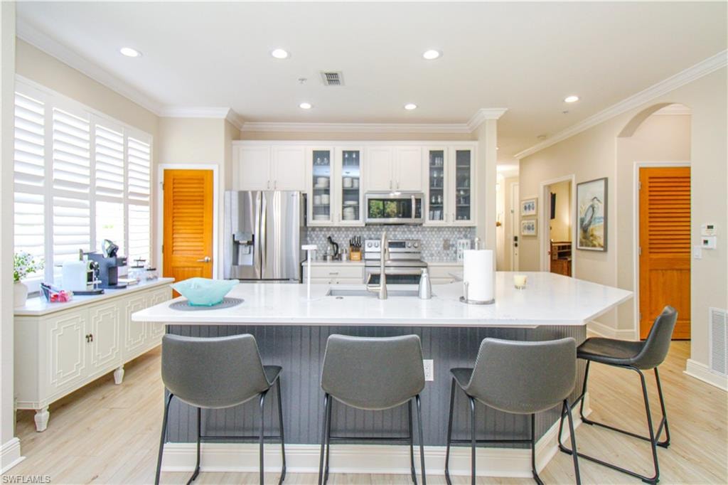 Kitchen with a large island, appliances with stainless steel finishes, white cabinetry, and light wood-type flooring