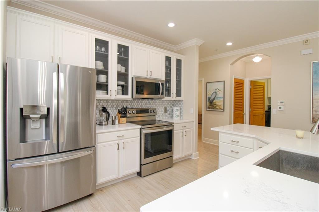 Kitchen with decorative backsplash, white cabinetry, stainless steel appliances, and sink