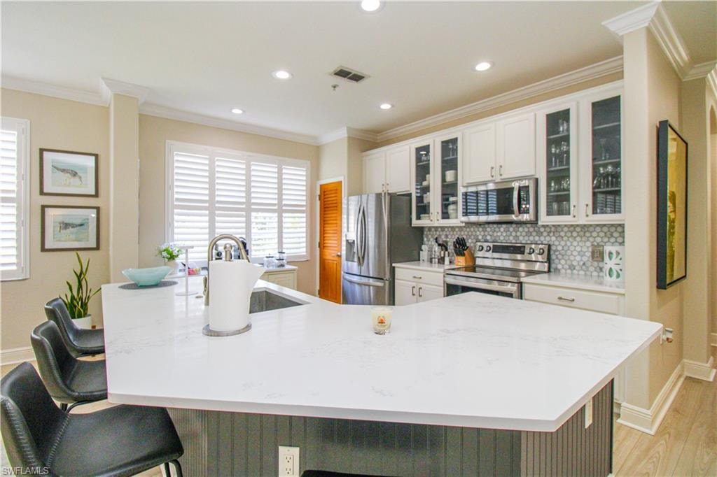 Kitchen with stainless steel appliances, a large island, a kitchen bar, white cabinetry, and light hardwood / wood-style floors