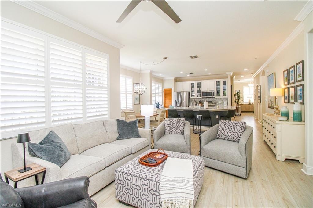 Living room with crown molding, light wood-type flooring, and ceiling fan with notable chandelier