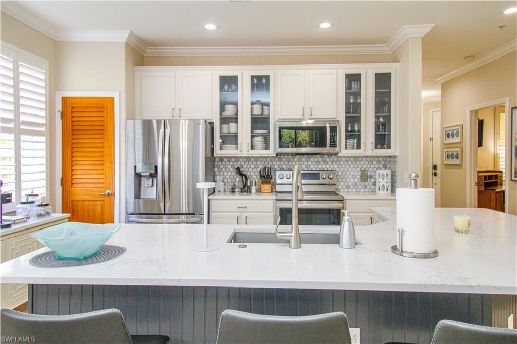 Kitchen featuring ornamental molding, decorative backsplash, appliances with stainless steel finishes, and a kitchen bar