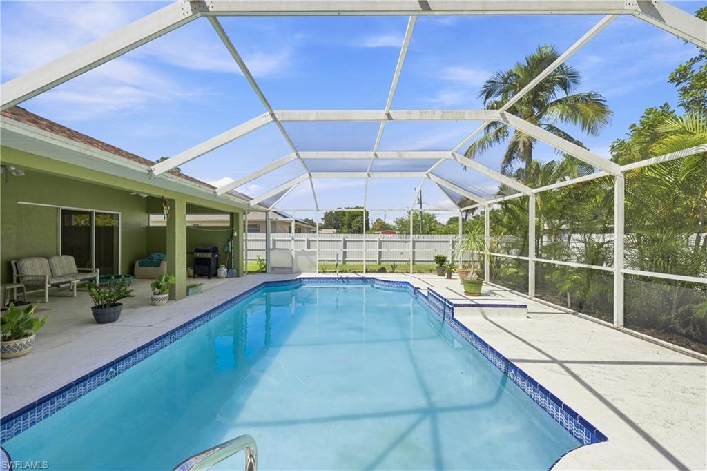 Screened-in outdoor living space featuring an in-ground swimming pool with tiled coping, a covered patio area, and a white privacy fence