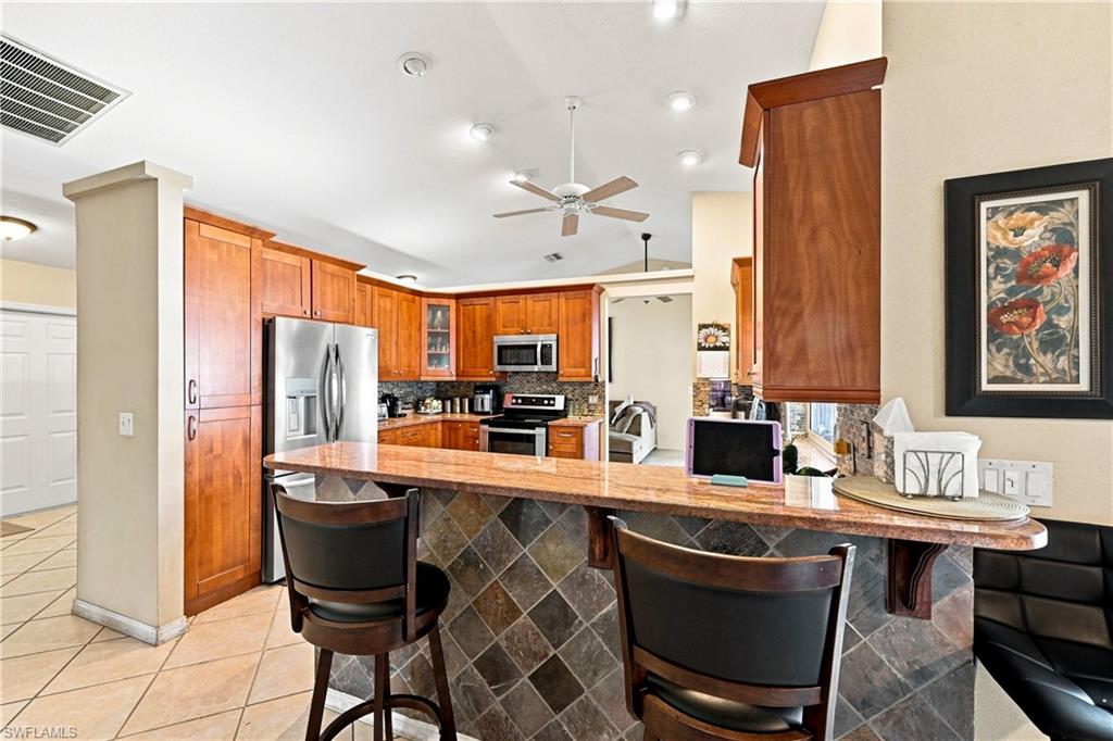 Kitchen featuring wood cabinetry, stainless steel appliances, a breakfast bar with stone tile fascia, and recessed lighting