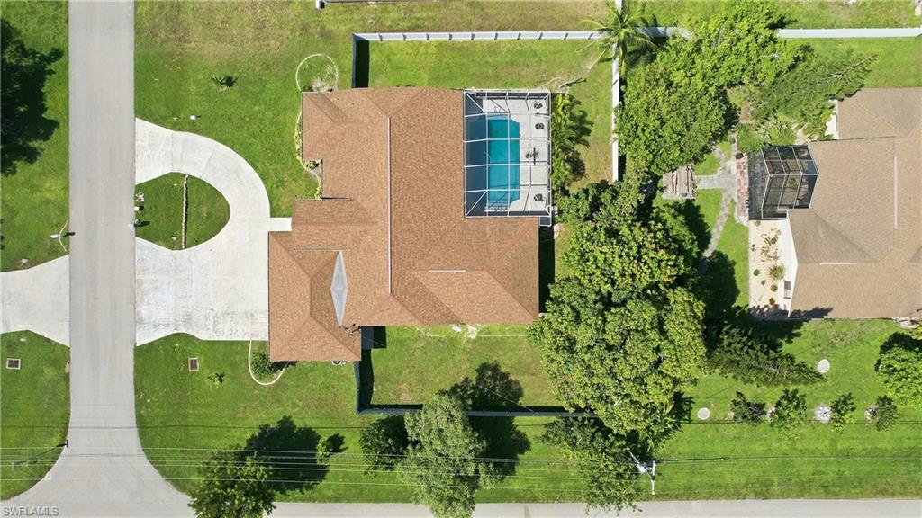 Circular driveway, screened-in swimming pool, shingle roof, mature landscaping, and green lawn