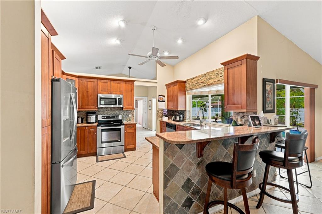Kitchen featuring wood cabinetry, stainless steel appliances, a tiered granite-finish counter, and tile flooring