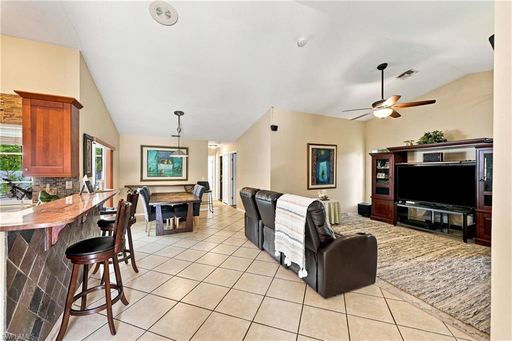 Vaulted ceilings, tiled flooring, wood-finish cabinetry, and a ceiling fan with integrated lighting