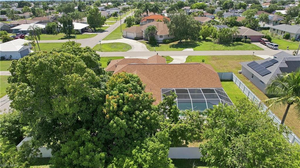 Screened swimming pool with a brown shingle roof, mature trees, and a paved driveway