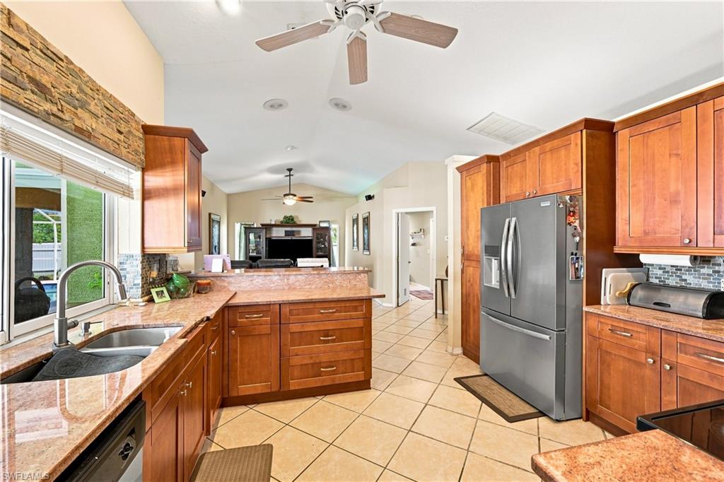 Kitchen featuring wood-finish cabinetry, granite countertops, tile flooring, stainless steel appliances, and a stacked stone accent wall