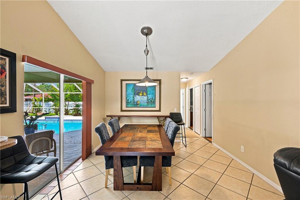 Vaulted ceiling with a pendant light fixture, tile flooring, glass sliding doors, and a swimming pool