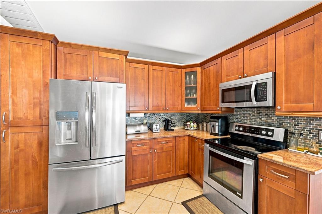 Wood-finish cabinetry paired with stainless steel appliances, mosaic tile backsplash, and light-toned countertop surfaces