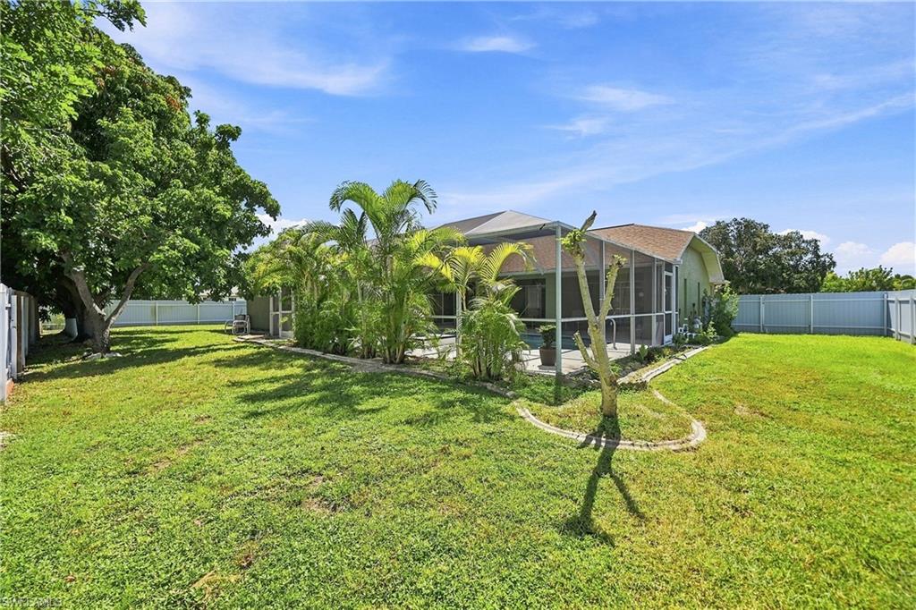 Expansive backyard featuring a screened-in lanai, mature landscaping, and a privacy fence