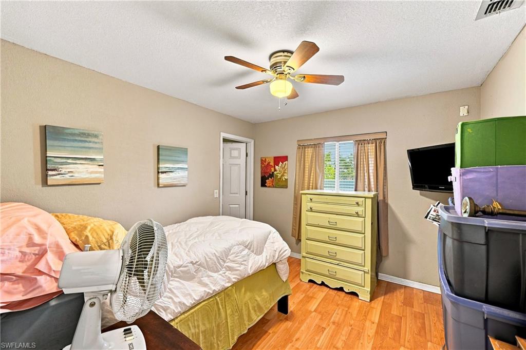 Wood-finish flooring, ceiling fan with integrated lighting, window with blinds and curtains, and a solid interior door