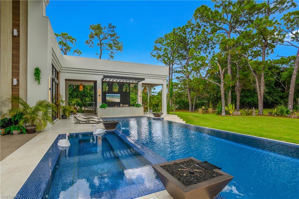 Custom pool with integrated spa, surrounding patio, outdoor living area with pergola, lush lawn, and mature trees
