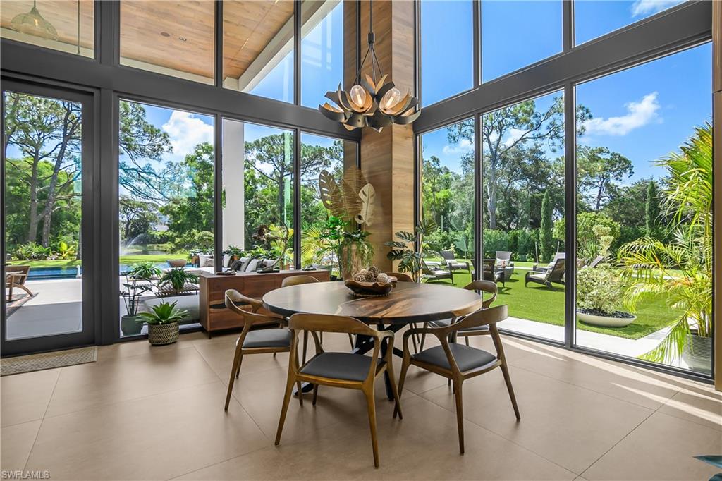 Expansive floor-to-ceiling windows, soaring ceilings, contemporary chandelier, wood-finish accent wall, and neutral tile flooring