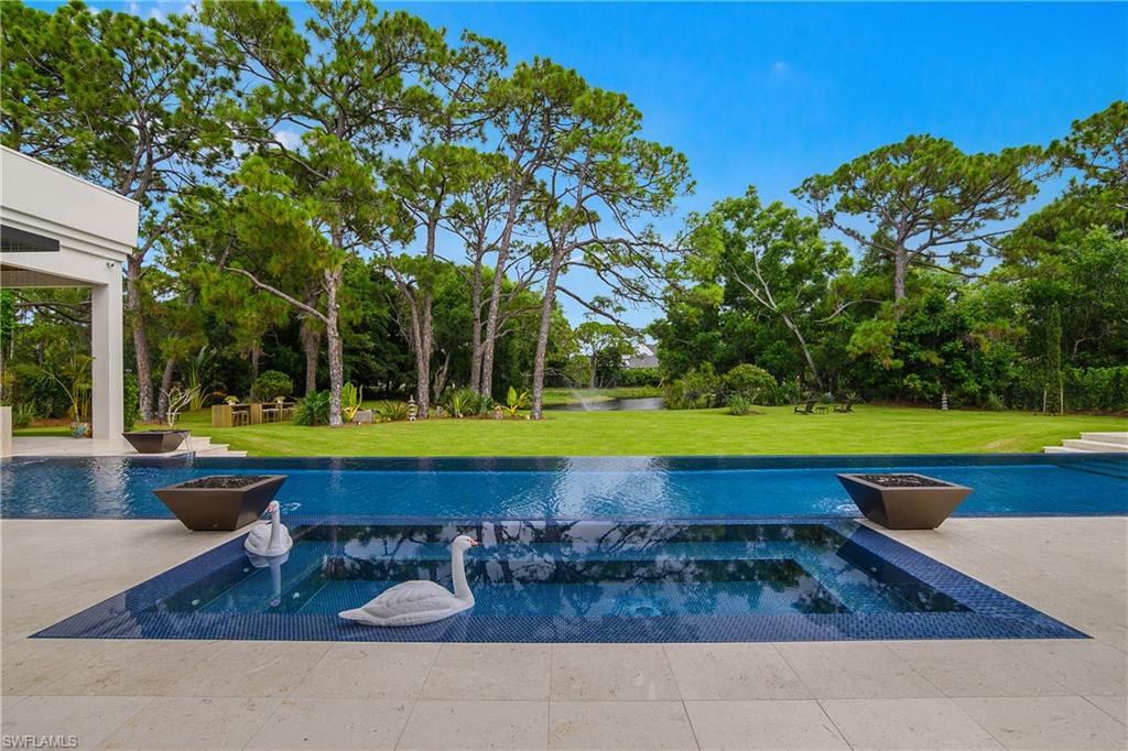 Expansive outdoor living area featuring a swimming pool, integrated spa, and tiled patio