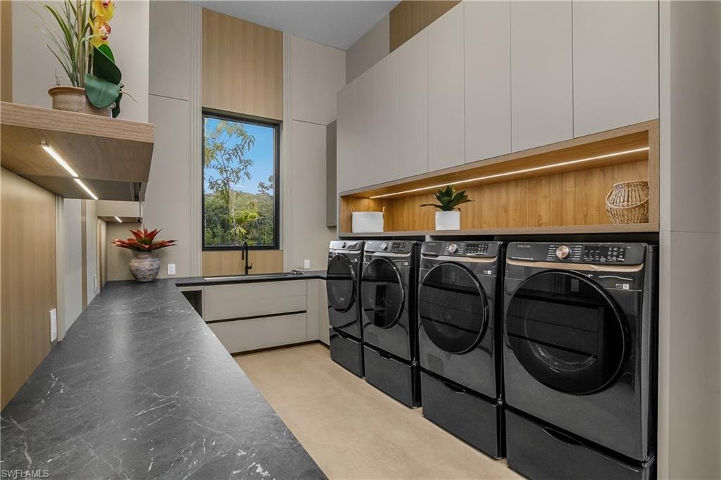 Sleek laundry area featuring a black-veined countertop, integrated sink with a black faucet, light wood-finish cabinetry, and overhead lighting