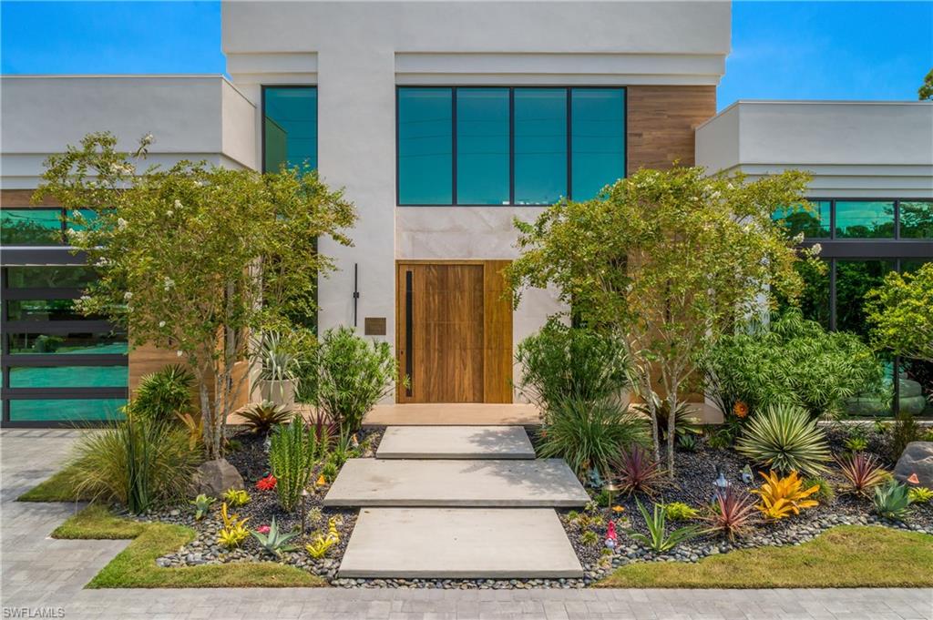 Modern exterior with a light-colored stucco finish, large glass windows, a wood-paneled entry door, and a glass-paneled garage door