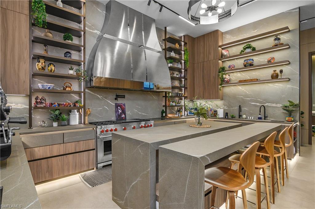Contemporary kitchen featuring a stainless steel range hood, integrated appliances, and a sprawling waterfall-edge island with stone countertops