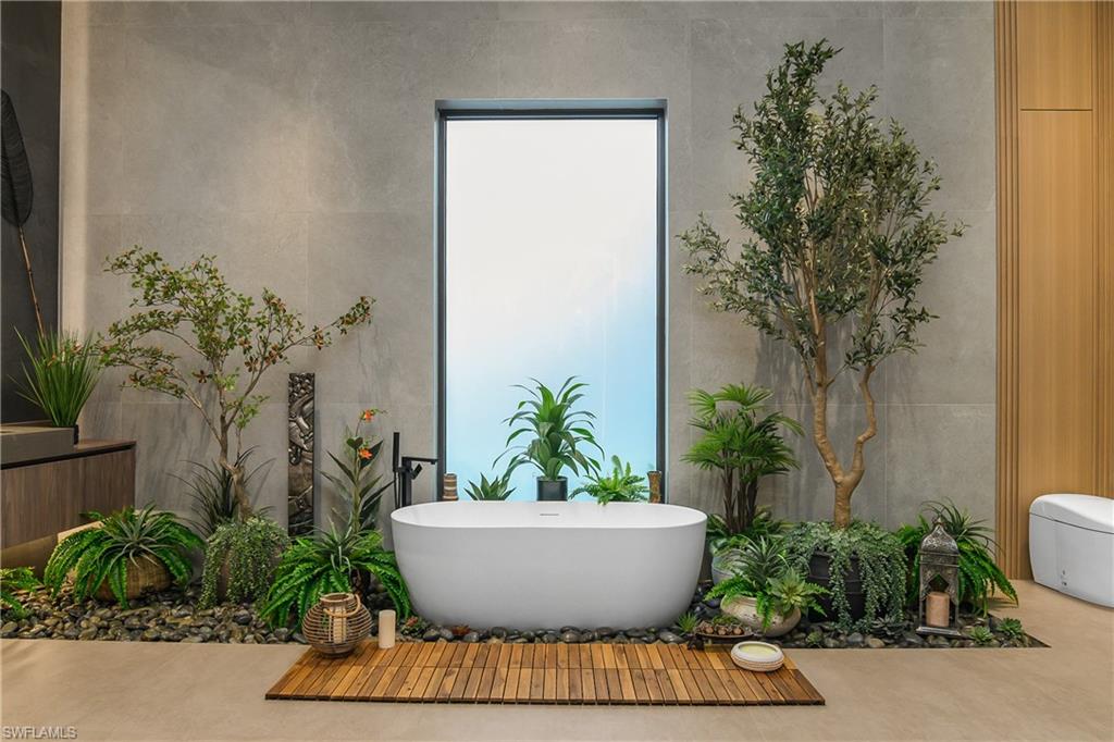 Freestanding soaking tub with a floor-mounted faucet, surrounded by an interior garden with varied plantings set on river rock