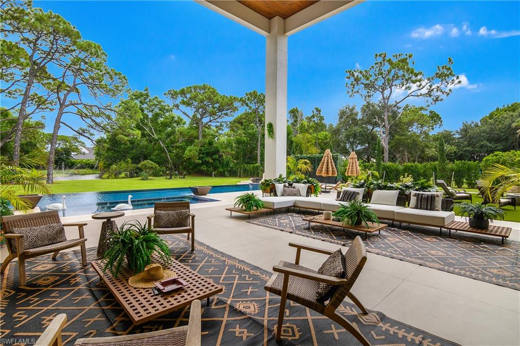 Expansive outdoor living area featuring a large covered patio, an integrated swimming pool, surrounding lush landscaping, and a manicured lawn