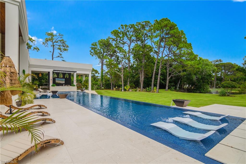 Infinity-edge pool with mosaic tile, spacious pool deck, covered outdoor living area, and expansive green space