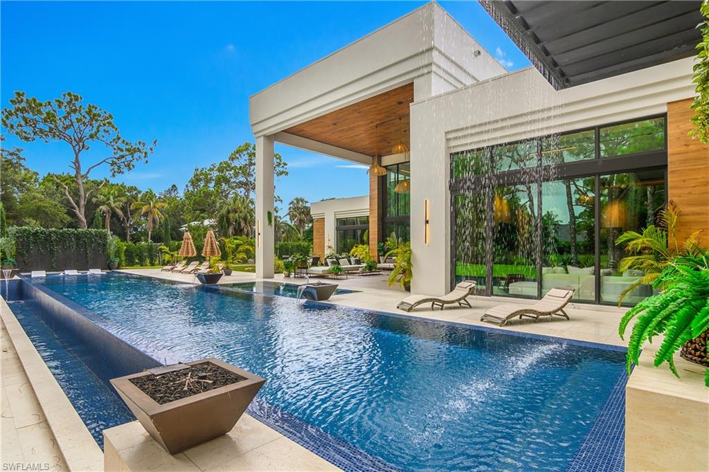 Modern exterior featuring a large swimming pool with mosaic tile accents, a covered patio with wood-finish ceiling, and expansive glass doors