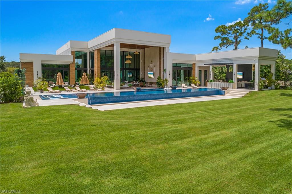 Modern architecture with expansive windows, an infinity-edge pool, an integrated spa, and an outdoor kitchen area