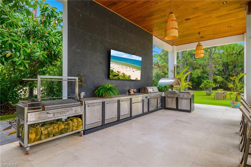 Expansive outdoor kitchen featuring a wood-finish ceiling, large format tile flooring, built-in stainless steel appliances, and a pizza oven