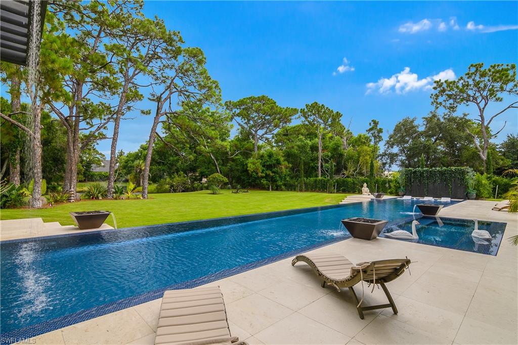 Expansive outdoor living area featuring a large swimming pool, integrated spa, and tiled patio