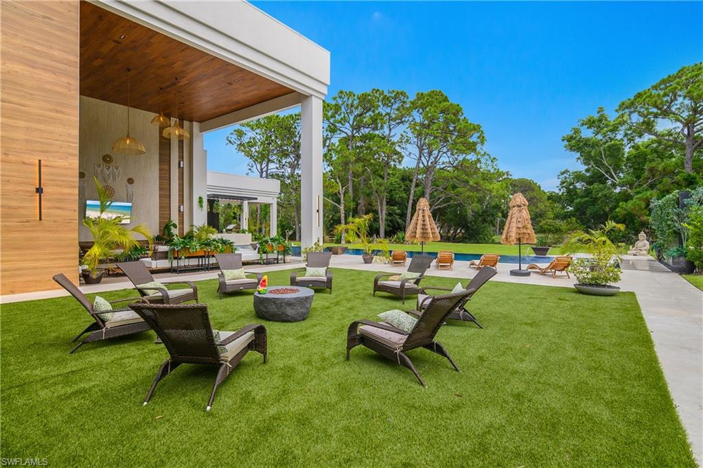 Expansive lawn area featuring a stone fire pit, covered patio with wood-paneled ceiling, and a swimming pool with surrounding hardscaping