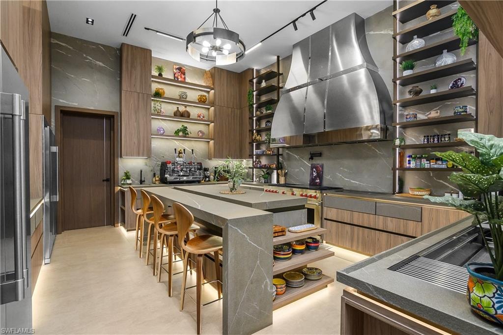 Gourmet kitchen featuring a large island, integrated appliances, wood-finish cabinetry, stone slab backsplash, and open shelving with integrated lighting