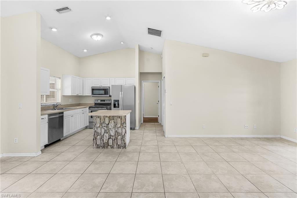 Kitchen featuring white cabinetry, stainless steel appliances, a center island with a stone-finish facade, and tile flooring