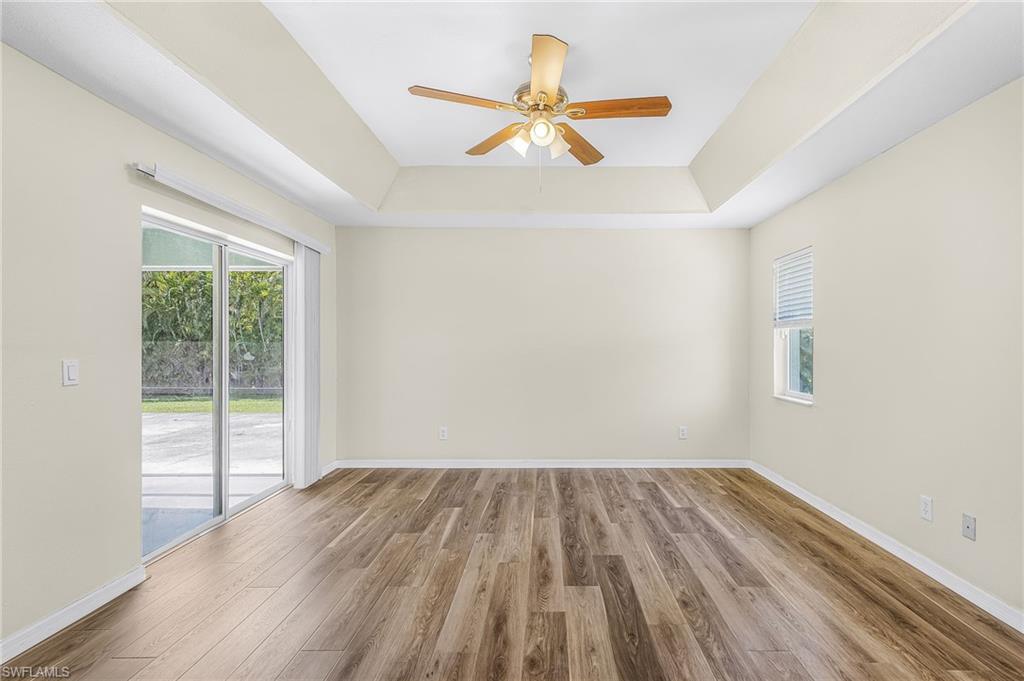 Tray ceiling, wood-finish flooring, ceiling fan, sliding glass door, and a window with blinds