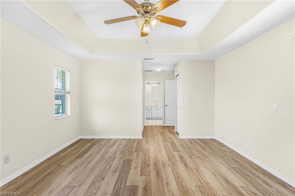 Tray ceiling with ceiling fan, wood-finish flooring, and a window with blinds