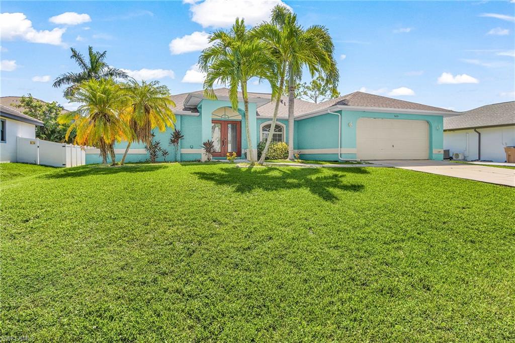 Tropical-inspired architecture featuring a turquoise exterior, double front doors, an arched entry, a two-car garage, and mature palm landscaping