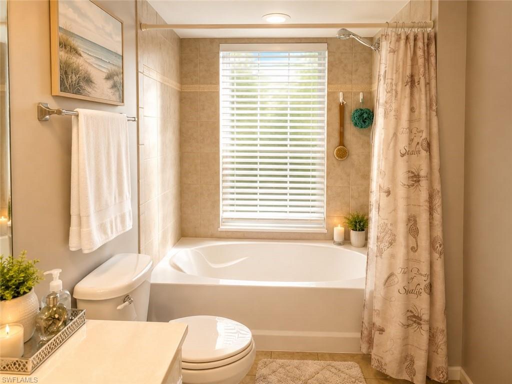 Built-in bathtub with tiled surround, a privacy window with blinds, and a mounted showerhead