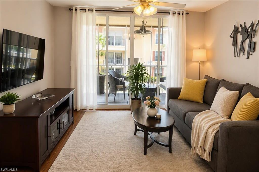 Sliding glass doors leading to a balcony, ceiling fan with integrated lighting, wall-mounted television, and a wood-finish media console