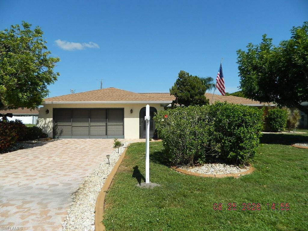 Exterior featuring a tan stucco finish, brown shingle roof, arched entry, and a paver driveway