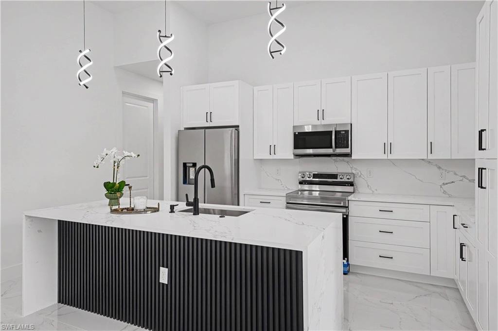 Kitchen featuring a waterfall-edge island with a black slatted base, stainless steel appliances, white cabinetry with black hardware, and pendant lighting