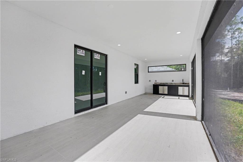 Modern open-concept space featuring polished concrete flooring, recessed ceiling lighting, and dual glass doors with dark frames opening to outdoor areas