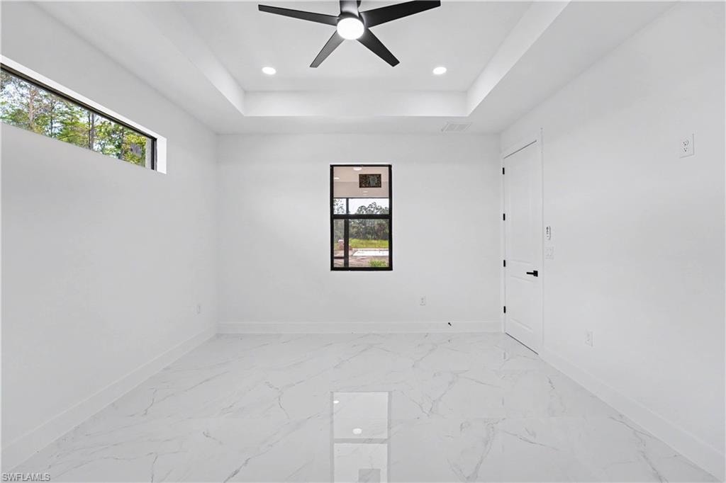 White large format tile flooring, tray ceiling with recessed lighting, black ceiling fan, and modern black-framed windows