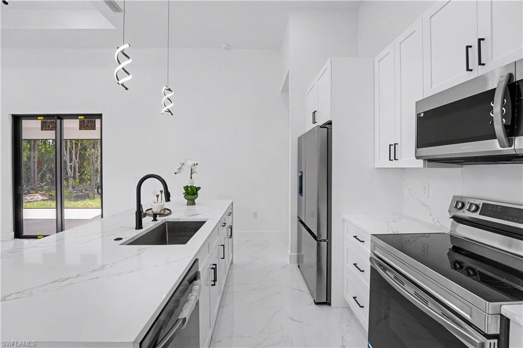 Kitchen island with integrated sink and matte black faucet, white cabinetry with black hardware, stainless steel appliances, and white marble-finish countertops