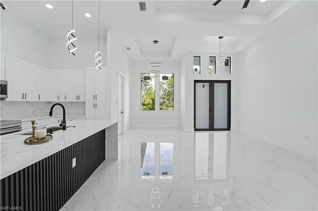Open-concept interior featuring high ceilings, white cabinetry, a kitchen island with a waterfall countertop, and large format polished tile flooring