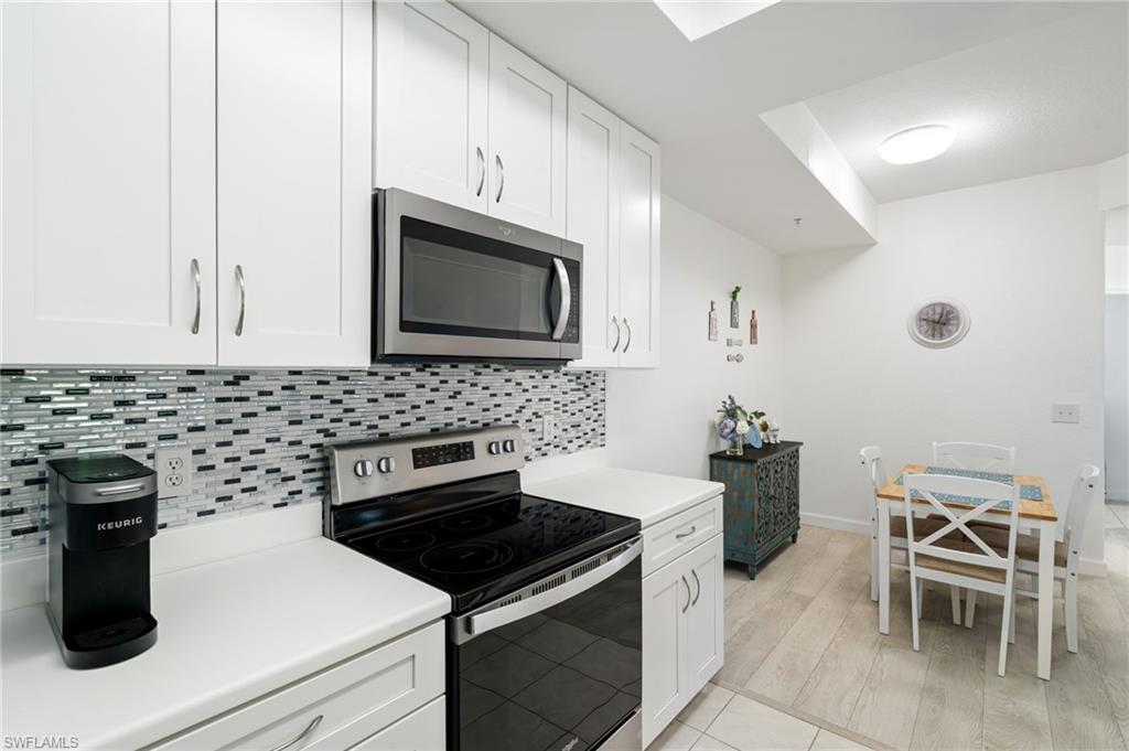 White cabinetry, stainless steel microwave, electric range, mosaic tile backsplash, and light-toned flooring