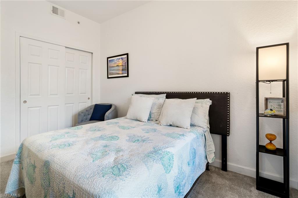 White paneled closet doors, dark upholstered headboard with nailhead trim, light gray carpeting, and white walls