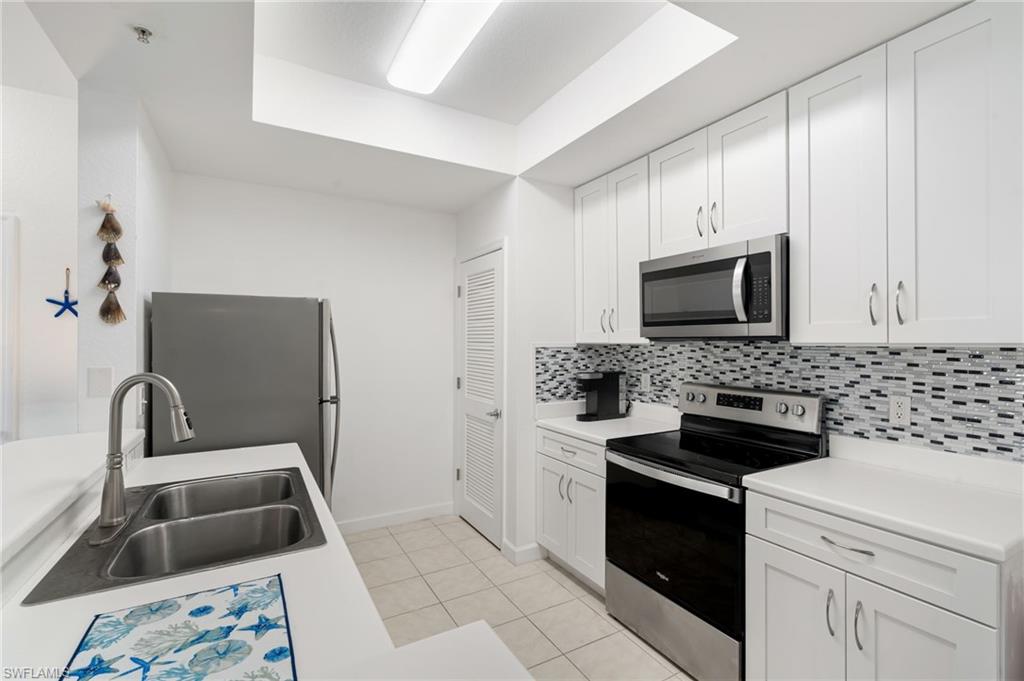 Kitchen featuring stainless steel appliances, white cabinetry, a dual basin sink, and a mosaic tile backsplash