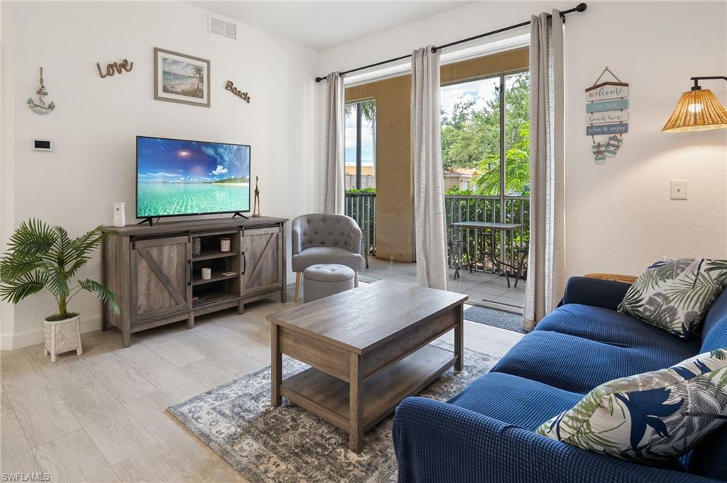 Light wood-finish flooring, sliding glass doors, built-in media console with barn-door style fronts, and balcony access